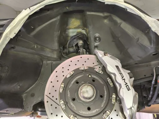 Unterbodenschutz entfernen am Mercedes W202 C55 AMG: Radhaus und Bremsscheibe vor der Behandlung, alter dunkler Unterbodenschutz sichtbar