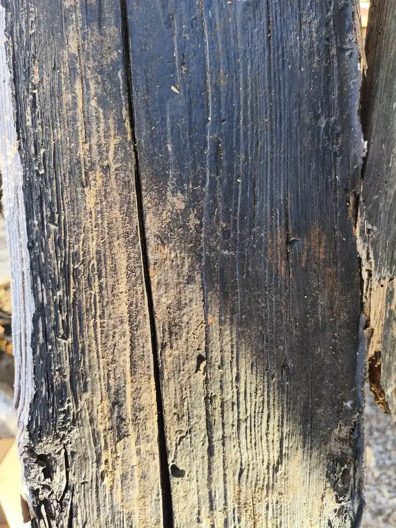 Probestrahlfläche beim Trockeneisstrahlen auf Holz an einem schwarz gestrichenen Balken, außen die alte Farbe, in der Mitte das freigelegte Holz