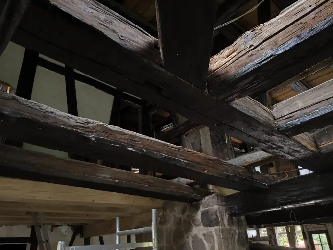 Vor dem Trockeneisstrahlen auf Holz: schwarz gestrichene Deckenbalken über einem Steinpfeiler