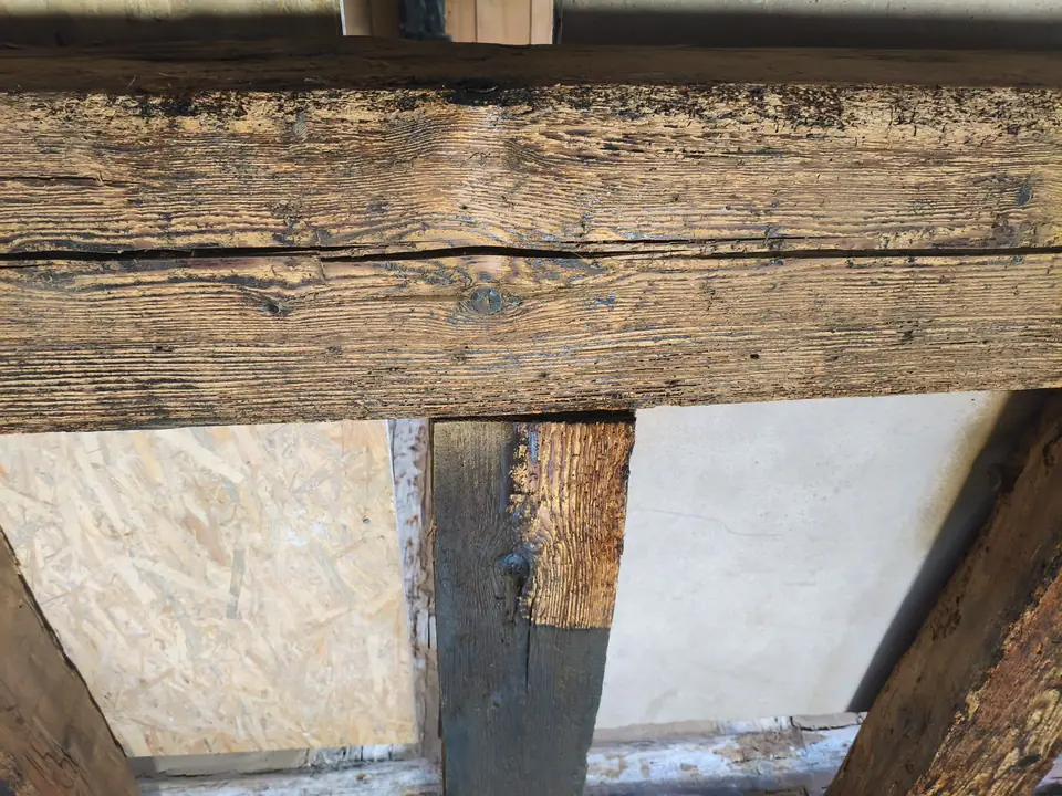 Trockeneisstrahlen auf Holz an einem Pfosten: oben hell freigelegtes Holz, unten noch die dunkle Farbe mit scharfer Grenze