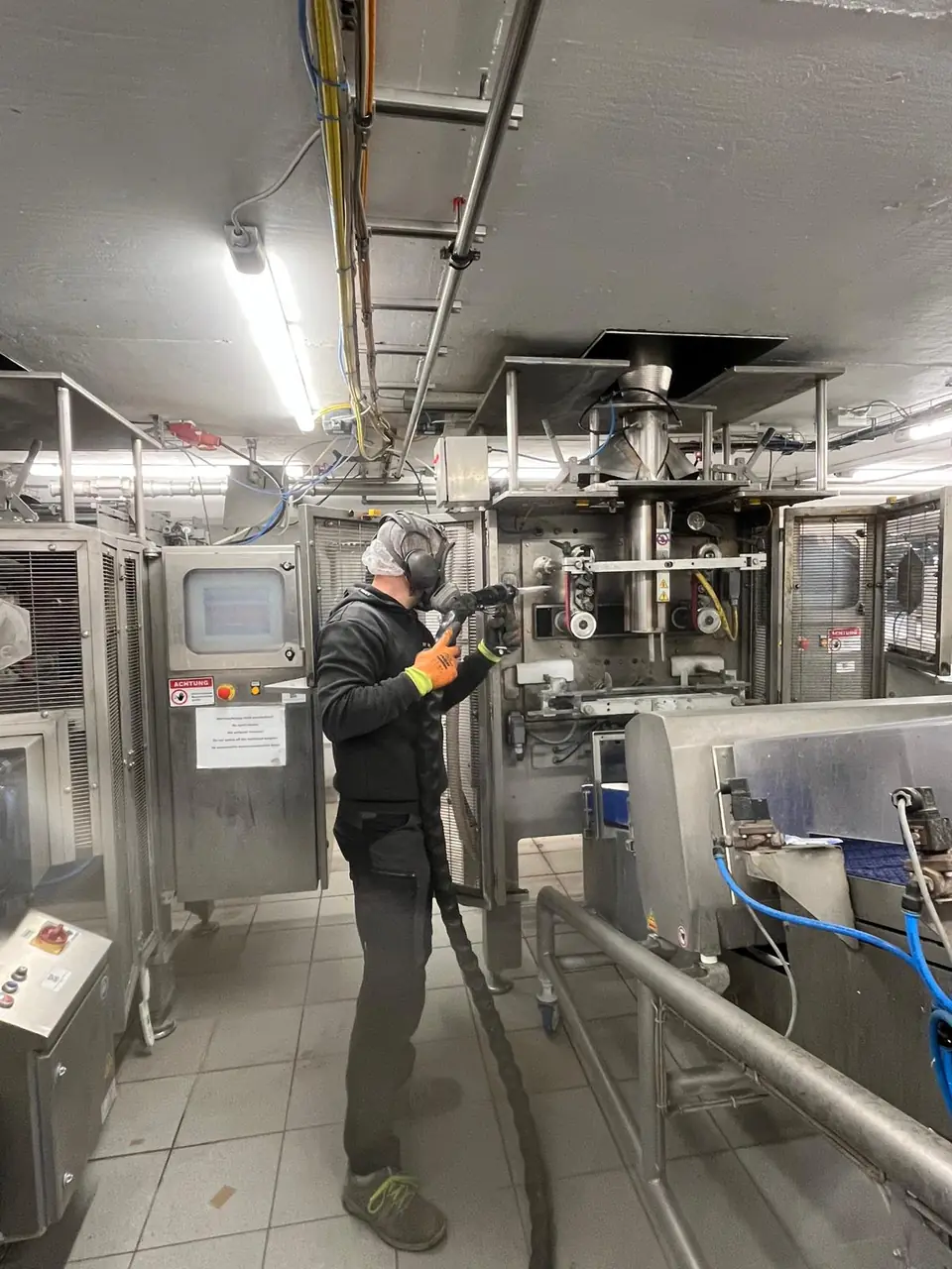 Industriereinigung in der Lebensmittelindustrie: Trockeneisstrahlen mit Vollmaske und Gehörschutz an einer Produktionsmaschine
